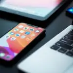 An iPhone 11 laying face up on a desk, next to a MacBook and an iPad