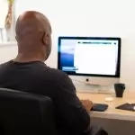 A person sitting at a desk, with headphones connected to the iMac they're using voiceover on.