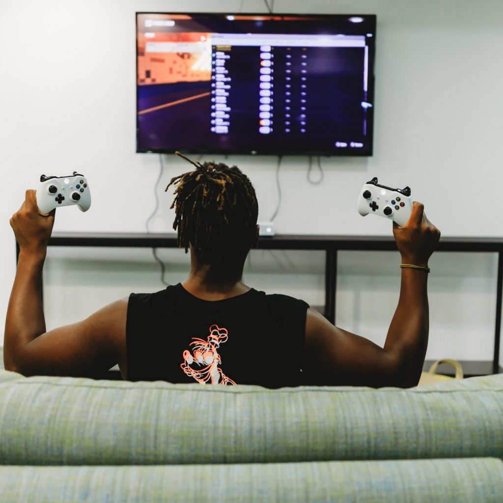 A person sitting on a couch, holding an Xbox controller in each hand