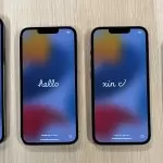 The iPhone 13 series face up on a desk, open to the start up screen with hello in a different language on each iPhone screen.
