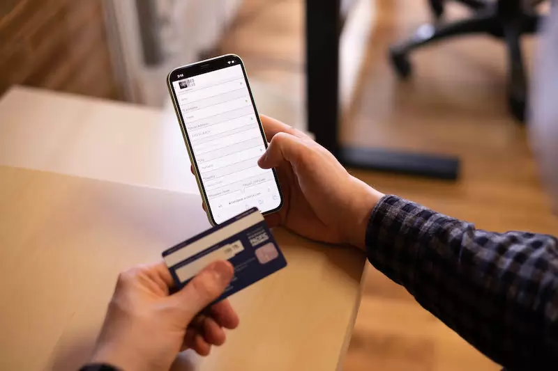 A person holding a credit card and a smartphone, using an e-commerce app, which must be tested for functionality.