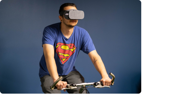 Tester riding a stationary bicycle while wearing a VR headset