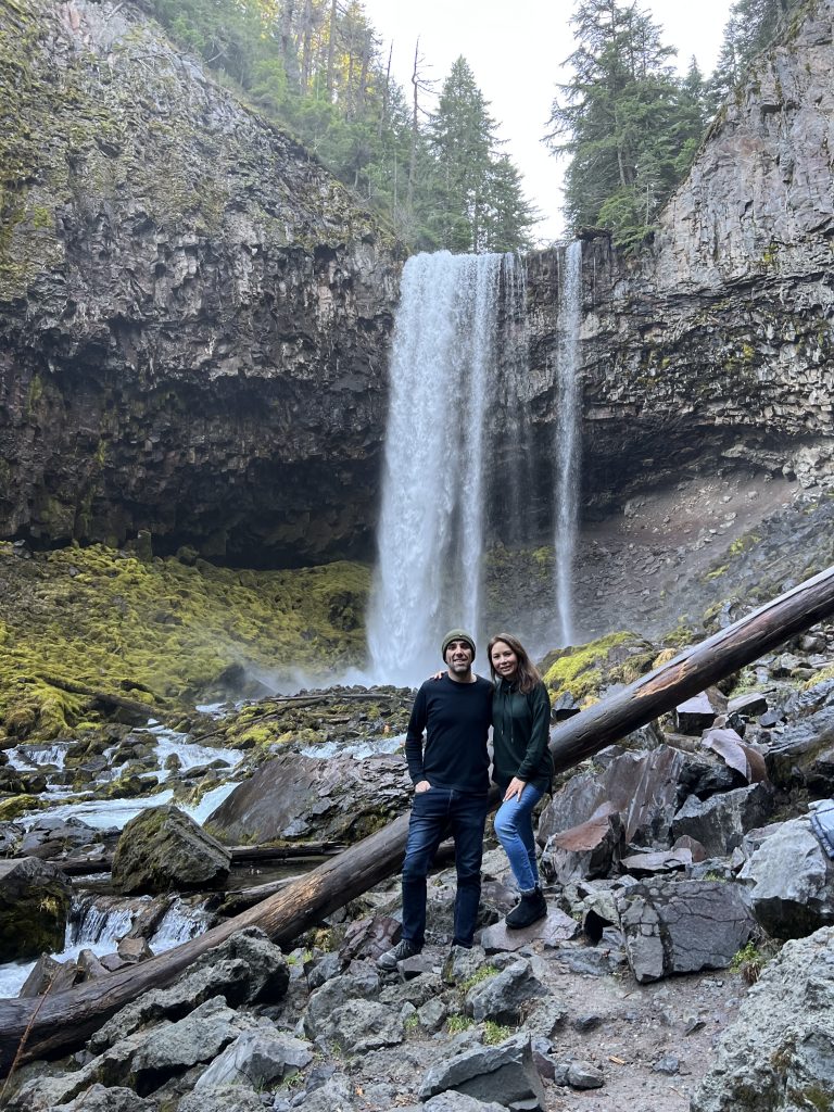 Audrey and Manu, partners at PLUS QA standing in front of a waterfall in the forest.