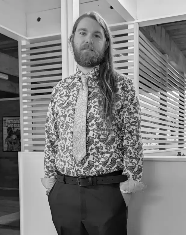 Brandon wearing a fancy shirt and tie and posing near the front of PLUS QA's office.